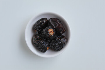 Five pieces of ajwa dates or ajwa khajur, in small bowl, isolated on white background, flat lay or top view