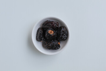 Five pieces of ajwa dates or ajwa khajur, in small bowl, isolated on white background, flat lay or top view