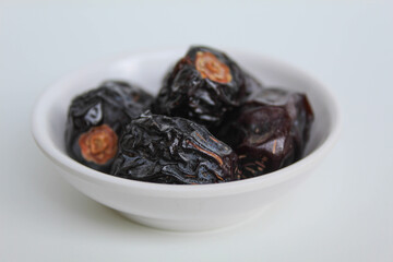 Five pieces of ajwa dates or ajwa khajur, in small bowl, isolated on white background