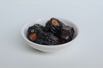 Five pieces of ajwa dates or ajwa khajur, in small bowl, isolated on white background