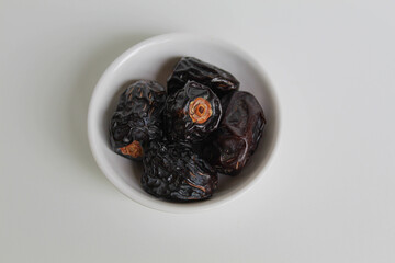 Five pieces of ajwa dates or ajwa khajur, in small bowl, isolated on white background