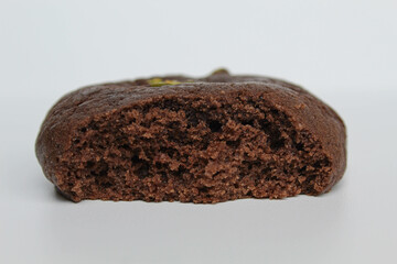 A bitten chocolate soft cookie, with green pistachio topping, isolated on white background