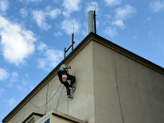 Worker in full safety gear performs high altitude facade work using industrial climbing equipment,...
