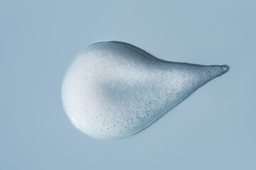 Cleansing foam drop smear with fine bubbles on blue background, symbolizing skincare, freshness and gentle facial hygiene