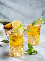 Two glasses with iced drink with lemon and mint on a light background with shadows