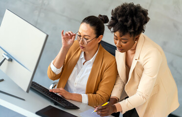 Two female entrepreneurs using computer for a productive business meeting in a corporate workplace.