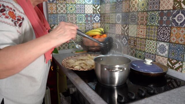 Cook the dumplings, take Varenyky out of the pan. Elderly woman cooking ah home kitchen. A saucepan of boiling water steams on the stove. Spoon in hand