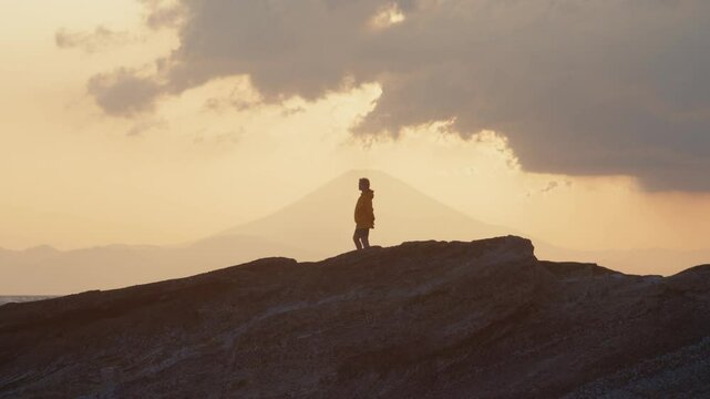 Peaceful Sunset Stroll by the Japanese Sea
Windy dusk on a rocky coast in Japan. A girl in a yellow jacket looks out at the horizon as soft blue light envelops the scene of the Fuji