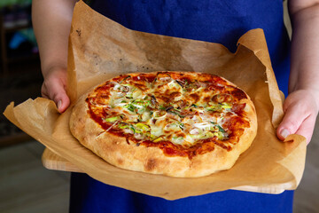 Fresh homemade pizza in the hands of the cook. Top view