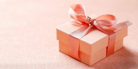 A peach-colored gift box adorned with a coral bow sits elegantly against a soft background, evoking feelings of celebration and anticipation