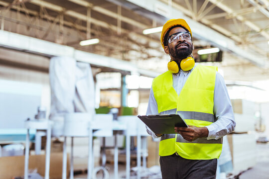Industrial Worker Inspecting Factory While Holding a Clipboard and Wearing Protective Gear