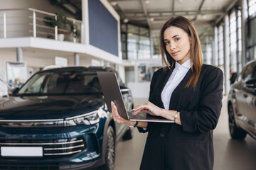 Saleswoman working on laptop in car dealership showroom