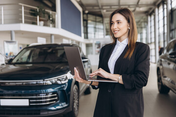 Saleswoman working on laptop in car dealership showroom