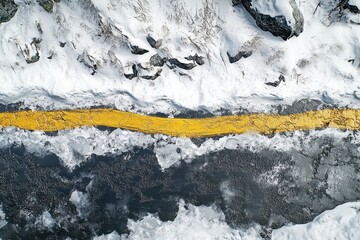 Fototapeta premium Aerial view of snowy mountain road with yellow line in winter. Use for travel, transportation, or winter hazard themes.