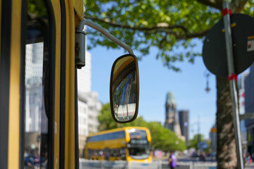 Bus mirror with Berlin backdrop. Side view of a yellow bus with a focus on the exterior mirror,...