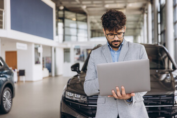 Car salesman working on laptop in car dealership showroom