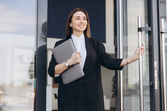 Businesswoman opening glass door holding laptop leaving office
