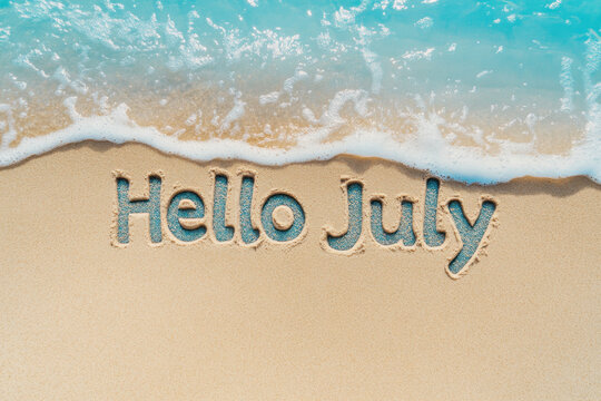 Hello july written on the beach sand with incoming wave