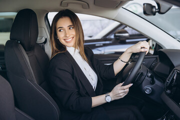 Businesswoman smiling and driving a new car in a dealership