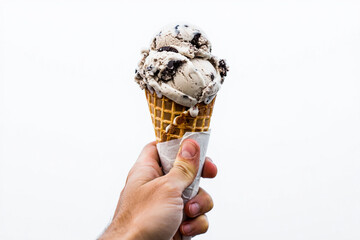 A hand holding a waffle cone filled with cookies and cream ice cream against a white background