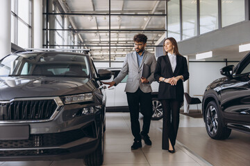 Car salesman showing new vehicle to female customer in dealership