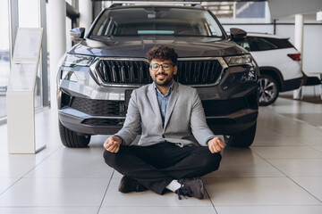 Salesman meditating in front of new car inside dealership