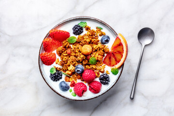 Granola with yogurt and fresh fruit. Organic gourmet muesli, overhead flat lay shot on a marble table, with a spoon
