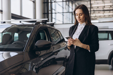 Saleswoman using smartphone next to new car in a dealership