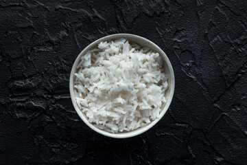 White rice, cooked. A bowl of boiled long grain rice, a simple side dish, overhead shot on a black background