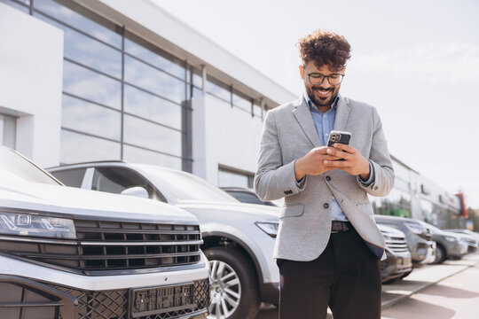 Salesman using phone in car dealership parking lot - Powered by Adobe