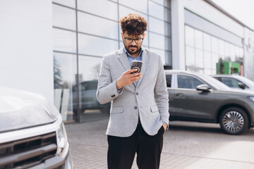 Businessman using smartphone and choosing new car in dealership