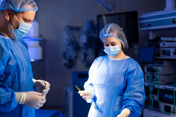 Surgeons operate in sterile room. Two surgeons in blue scrubs and masks focus on a surgical...