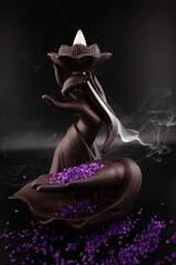 Obraz premium Ethereal scene of a backflow incense burner shaped as a hand holding a lotus with fragrant smoke cascading downwards amidst scattered purple sea salt Evokes mystery, tranquility and spiritual ambiance