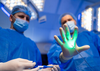 Surgeons using laser tech. Two surgeons in blue scrubs focus on a laser device during a surgical...