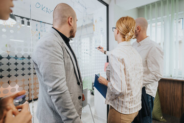 Obraz premium Colleagues participating in a business meeting, brainstorming and discussing strategies displayed on a whiteboard in a modern office space with a focused and collaborative atmosphere