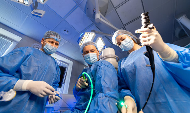 Team doing advanced procedure. Medical professionals in blue scrubs conduct a procedure using specialized instruments in a well-lit surgical room.