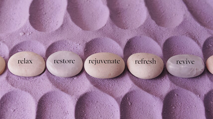 Smooth, pale stones with words relax, restore, rejuvenate, refresh, revive on lavender textured background, symbolizing wellness and serenity