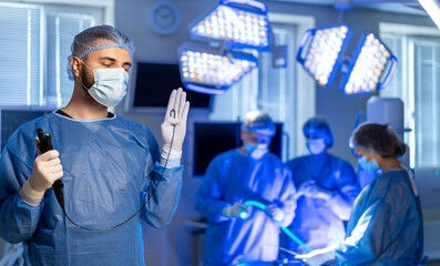 Surgeon readying for surgery. A surgeon stands ready in an operating room while colleagues set up for a complex surgery, focused on their tasks.