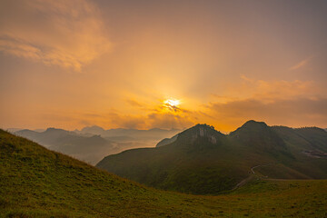 Aerial view of serene sunset casts a golden glow over rolling hills and distant mountain peaks,...