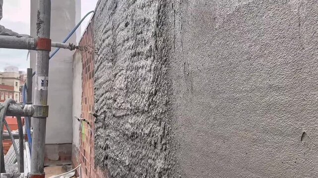 Worker spraying mortar onto a brick wall at a construction site