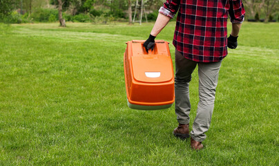 man in casual clothes holds bag with cut grass of lawn mower after mowing lawn with at own backyard. Husband takes care of garden. Modern gasoline garden equipment. Landscaping work at home
