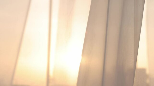 Light breezy sheer curtain blowing in the wind with sunset behind it