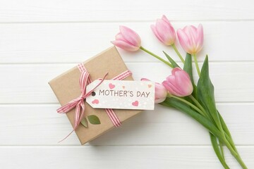 Happy Mother's Day tag attached to craft paper gift box with tulip flowers on white wooden background