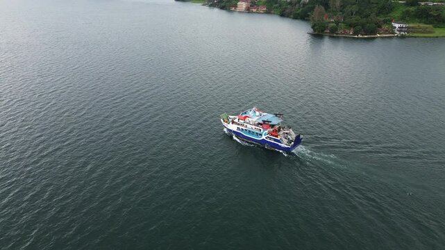Aerial view of ferry crossing Lake Toba from Parapat to Ambarita, Samosir Island, North Sumatra, Indonesia, with scenic cloudy sky and calm water reflection