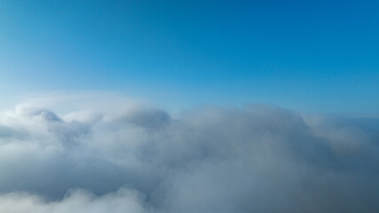 A serene view of the early morning sun rising above a vast sea of clouds, with distant mountain peaks faintly visible on the horizon, creating a peaceful and ethereal landscape. Flying over the cloud