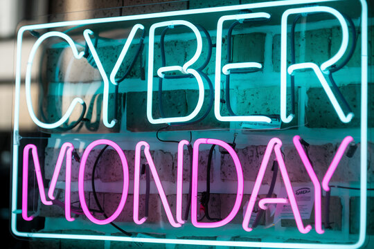 Neon sign displaying "Cyber Monday" in teal and pink lettering against a brick wall, showcasing a retail sales promotion
