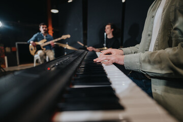 Band members rehearse with instruments including a piano, bass guitar, and drum set in a studio....