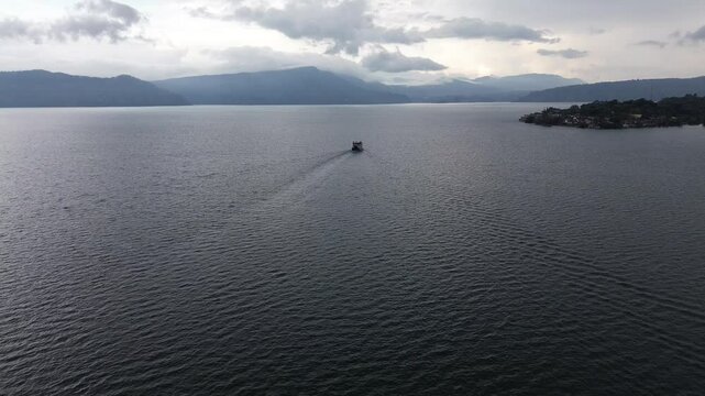 Aerial view of ferry crossing Lake Toba from Parapat to Ambarita, Samosir Island, North Sumatra, Indonesia, with scenic cloudy sky and calm water reflection