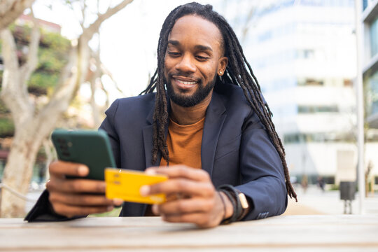 Businessman using smartphone and holding credit card outdoors