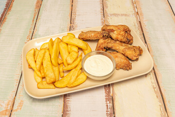 Fried chicken wings with sauce on a tray along with some French fries